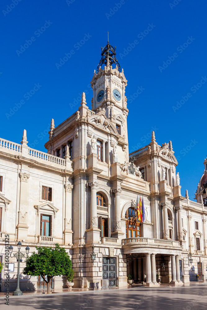 Obraz premium The City Hall in Alicante, showcasing intricate architecture with a prominent clock tower, standing under a clear blue sky, represents local governance and cultural heritage.