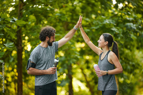 Billede på lærred Two active individuals share a joyful moment in a park, giving each other high fives after a workout session, showcasing camaraderie in their fitness journey and promoting a healthy lifestyle