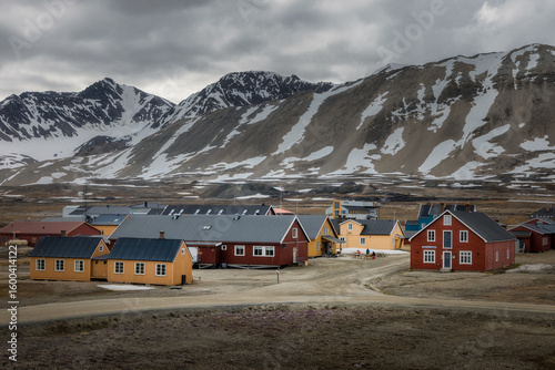 View of colorful houses nestled against the stark, snow-dusted mountains under a brooding sky, creating a striking contrast of warmth and wilderness, Longyearbyen, Svalbard and Jan Mayen.