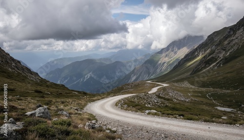 Winding mountain road covered in light green grass, surrounded by rocks, boulders. Cloudy sky adds tranquility to serene landscape. Perspective from side of road offers glimpse of path as meanders