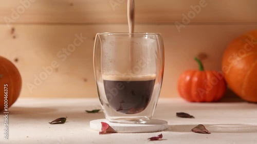 Brown sugar latte being mixed in double wall glass, cozy autumn scene with pumpkins and dry leaves, warm homemade seasonal coffee drink.
