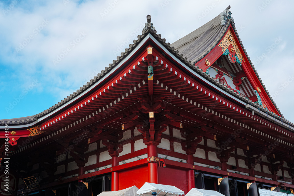 Fototapeta premium Close-up of a traditional Japanese temple roof with intricate red and white details against a blue sky with clouds.