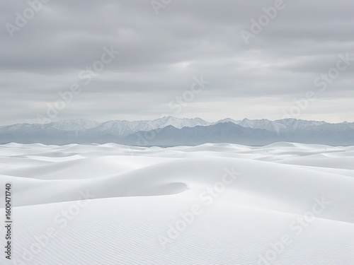 Serene view of white sand dunes under cloudy sky with distant mountain ranges in background