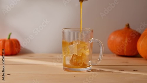 Golden pumpkin syrup is poured over ice in a clear glass mug, creating the cozy autumn mood for a homemade seasonal latte.