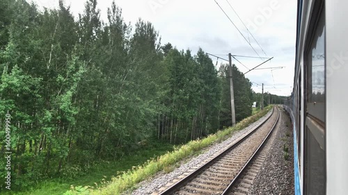 A train moves smoothly along winding tracks surrounded by vibrant greenery. The scene captures the tranquility of rural life and the beauty of nature on a cloudy day.