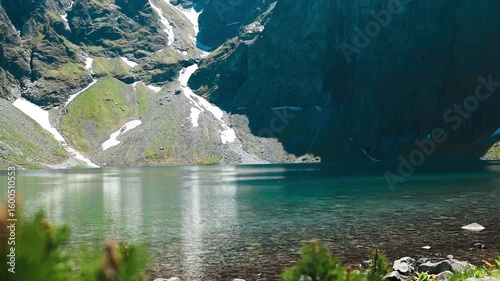 A stunning view of a clear alpine lake in the Tatra Mountains, Poland. Surrounded by rocky peaks and patches of melting snow, this peaceful landscape is perfect for nature, travel, and hiking visuals.