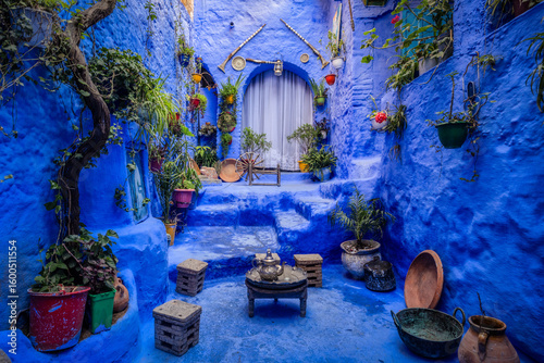 View of a mesmerizing blue-washed alleyway adorned with vibrant potted plants and rustic decor, inviting exploration into its depths, Chefchaouen, Tangier-TÃ©touan-Al Hoceima, Morocco.