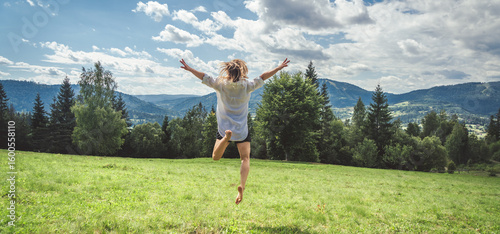Happy young woman jumping on the meadow in mountains.