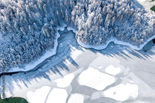 Aerial view of a winding frozen lake flanked by a dense, snow-covered forest. Aesthetic winter backdrop 