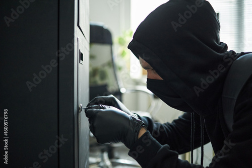 Photos Young masked male intruder wearing black hoodie and gloves picking lock on large