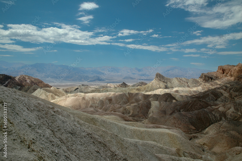 Fototapeta premium Vibrant multicolored hills and distant mountains in Death Valley under a clear sky, showcasing the dramatic geology of the desert landscape. A natural wonder shaped by erosion and time