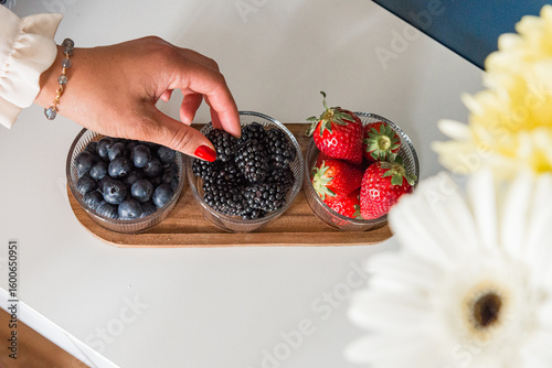 Foto une main de femme saisit une mure dans un plateau de fruits rouges comportant de