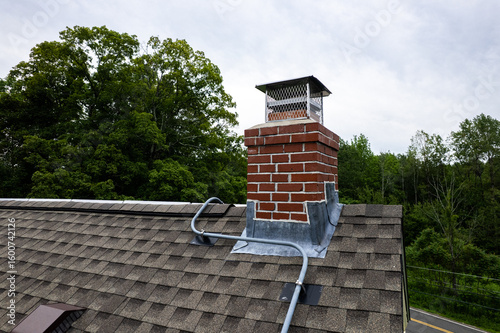 Close-up of Brick Chimney with Flashing and Electrical Conduit on Asphalt Shingle Roof