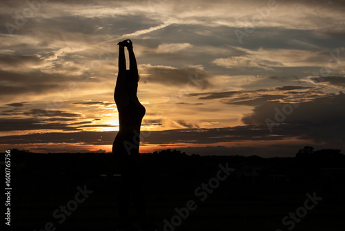 Silhouette of a plump young woman warming up before exercising for better health during sunset.