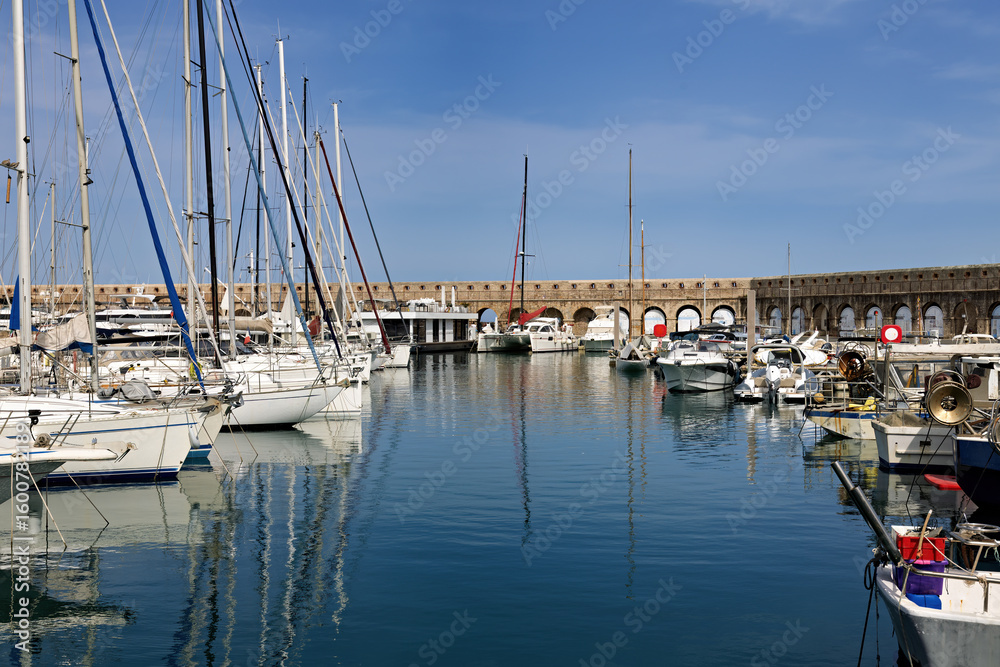 Fototapeta premium Marina with sailboats and yachts in Antibes on the Cote d'Azur with city walls and snow-capped mountains in the background, in spring