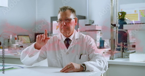 Senior scientist in lab coat pointing upward in research laboratory, with tablet computer on bench