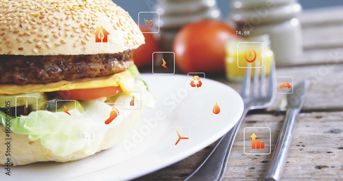 Showing sesame bun cheeseburger on white plate on table with floating digital icons, copy space
