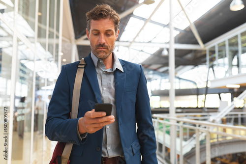 Wallpaper Mural Middle-aged man in suit using smartphone while leaning on railing inside transit hub Torontodigital.ca