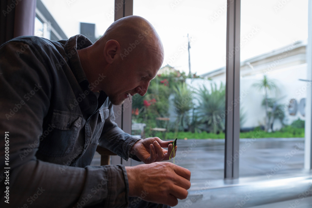 Naklejka premium Man examining plant cutting near sliding glass door, showcasing wet patio with potted succulents
