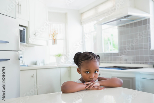 Child African American girl leaning on island looking thoughtful in kitchen near white cabinets