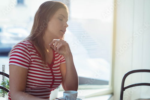 Free Download Woman sitting at cafe table by window resting chin on hand gazing over white coffee cup - GFXLoad