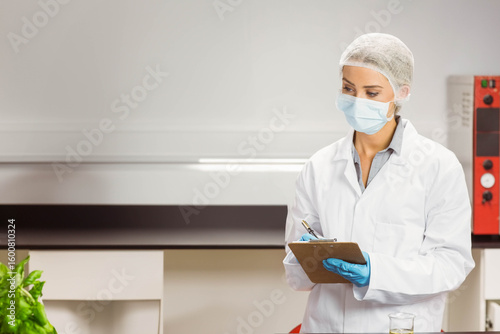 Clipboard and pen resting beside glass beaker with clear liquid on steel bench near incubator