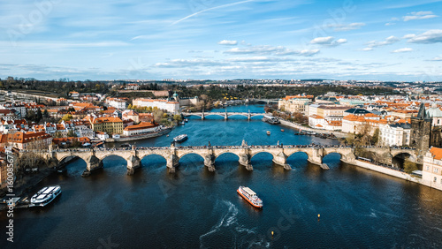 Aerial view of the iconic Charles Bridge gracefully arches over the Vltava River, connecting the old and new cities under a serene sky, Prague, Czechia.