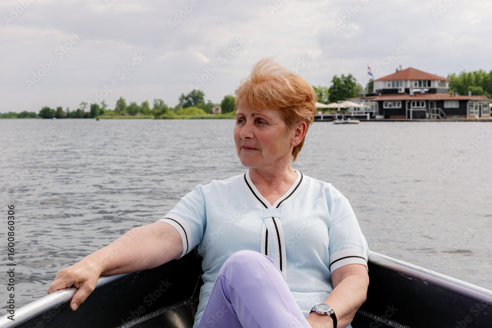 Fototapeta premium A beautiful grandmother is sailing in a boat on a lake in the countryside.