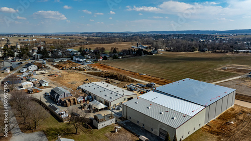In a developing rural area, a large warehouse is under construction next to small houses and farmland.