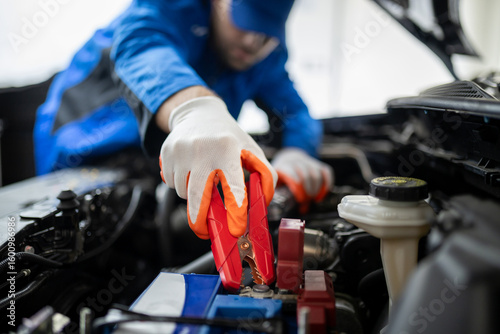 Car battery jump-start process performed by a mechanic in an auto repair shop during daylight hours