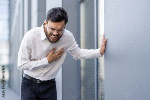 Photography A man in business attire clutches his chest, likely experiencing chest pain, reflecting possible health issues or stress in a professional environment
