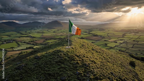Green rolling hill dramatically rising under gently waving irish national flag, revealing expansive sunlit valley representing peaceful rural irish landscape and national pride