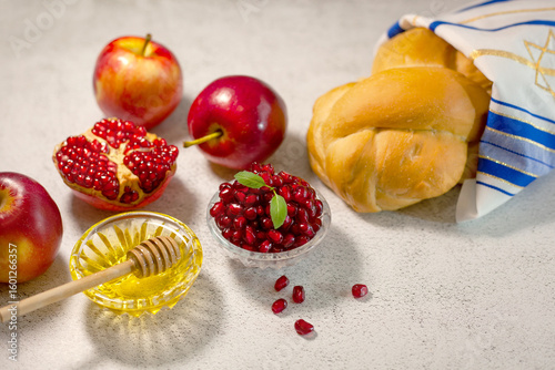 Rosh Hashanah, the Jewish New Year. Traditional symbols are tallit, apples, pomegranate, hala bread and honey on a light background. Happy Rosh Hashanah. Shana Tova