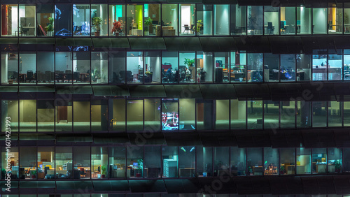 Working evening in glass office building with numerous offices with glass walls and windows timelapse