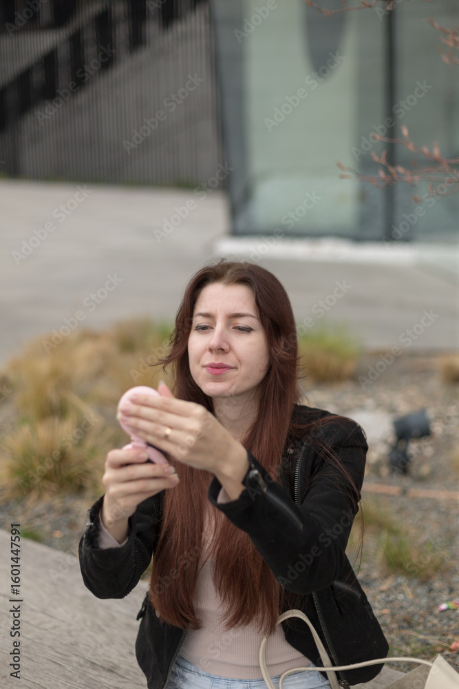Fototapeta premium A woman with long black hair is sitting comfortably on a bench, intently looking at her phone while enjoying the winter day
