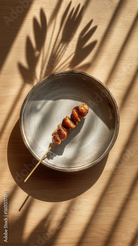 A skewer of grilled meat on a plate casting shadows on a wooden surface in the bright sunlight