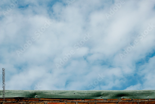 beautiful clear sky with white clouds, captured above a weathered brick wall with a green material atop.