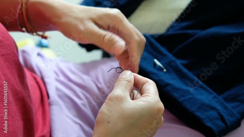 Caring mother repairing her child’s trousers by hand, focusing on sewing trouser legs.