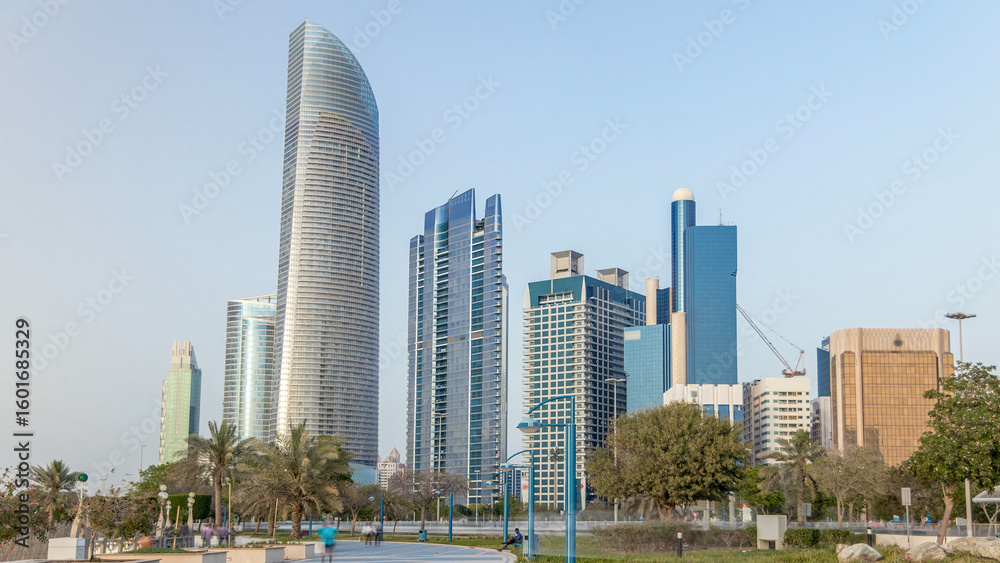 Obraz premium Corniche boulevard beach park along the coastline in Abu Dhabi timelapse with skyscrapers on background.