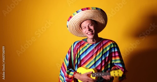 Happy man in sombrero hat and colorful poncho playing ukulele on yellow background. Space for text