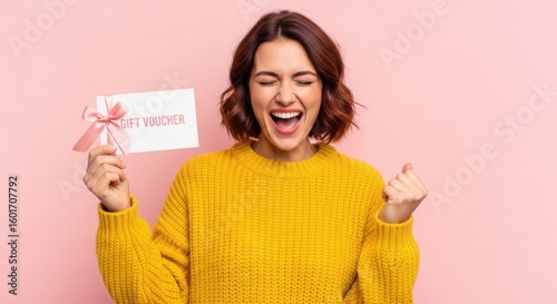 Ecstatic Woman Celebrates Winning Gift Voucher in Yellow Sweater on Pink Background