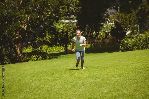 Child running barefoot across wide green lawn near trees shrubs and stone wall in garden