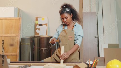 African American carpenter woman hammering a piece of wood for a chair in a woodworking shop. Skilled in crafting wooden furniture, craftsmanship in the workshop, DIY, National Carpenters Day