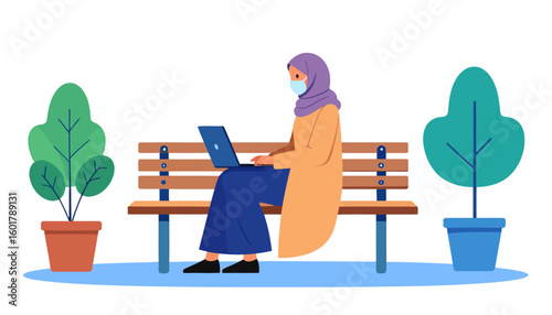 Muslim woman in a hijab and face mask working on a laptop, sitting on a wooden park bench.