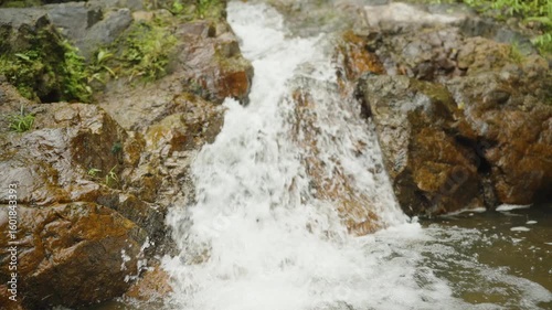 Clear stream of water cascading down mossy rocks in lush forest in slow motion, low angle, Nature Concept