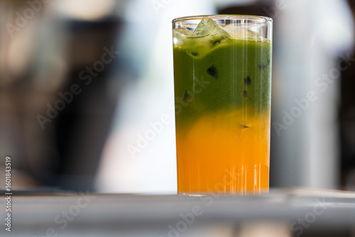 Close up and selective focus a glass of iced matcha latte separated layers with orange juice