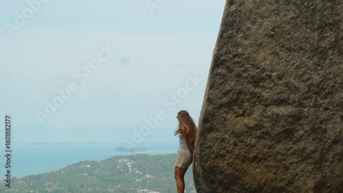 Young Woman Standing Against Huge Rock Looking Over Ocean View From Side Angle at Overlap Stone Samui, Nature Exploration Concept