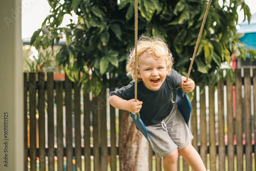 Happy little boy with big smile on backyard swing