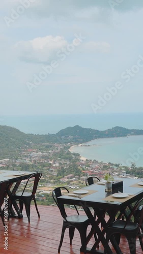 Vertical video. Elegant Outdoor Seating Area With Set Tables and Ocean View Surrounded by Green Hills From Elevated Angle at Overlap Stone Samui, Scenic Leisure Concept