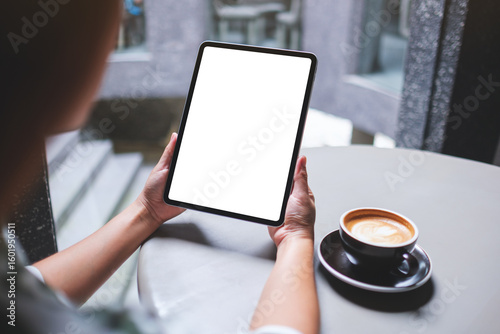 Mockup image of a woman holding digital tablet with blank white desktop screen in cafe